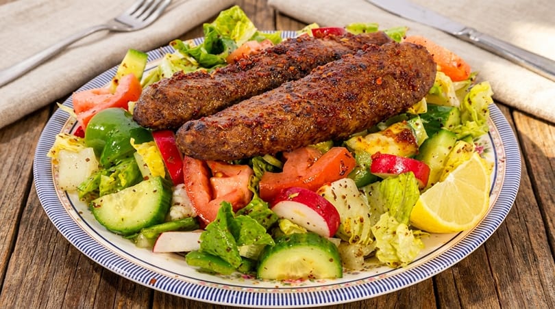Two seasoned meat kebabs on a fresh garden salad with a lemon wedge.