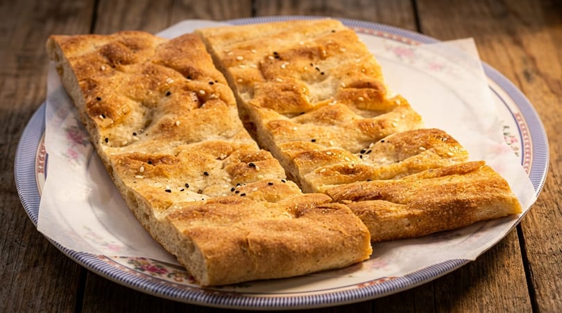 Golden flatbread pieces topped with sesame and black seeds, served on a plate on a wooden table.