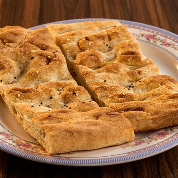 Two golden-brown flatbread pieces, sprinkled with sesame seeds, on a floral plate.