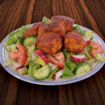 Grilled lamb kofta meatballs over salad on a dark wood table